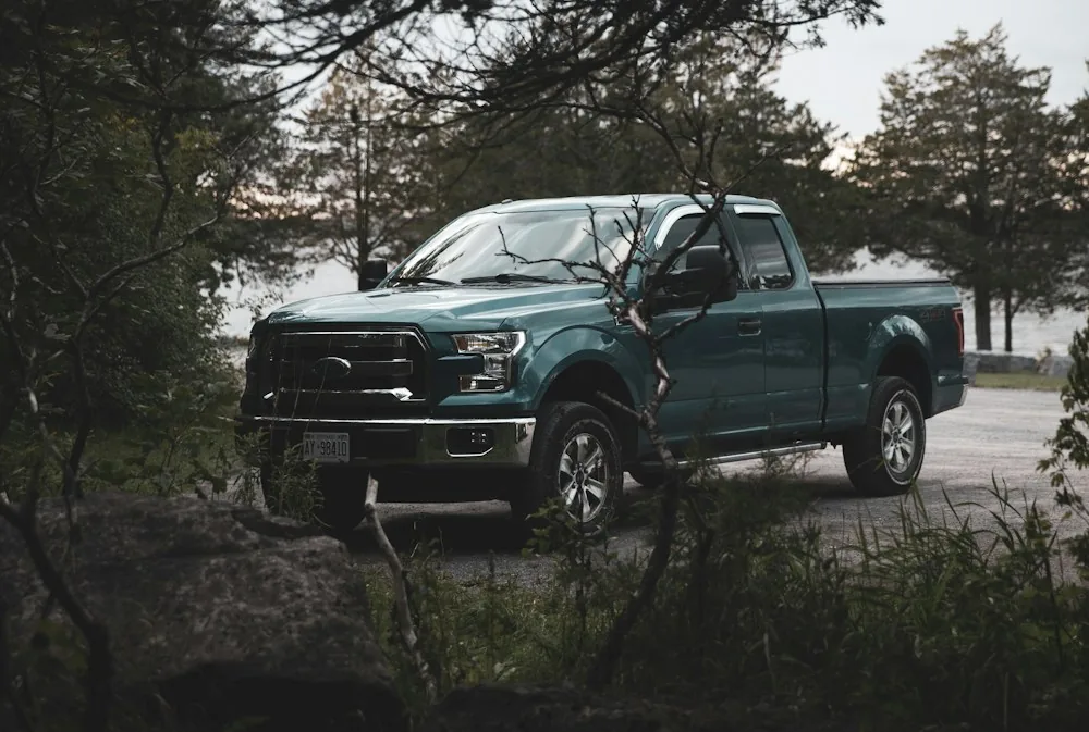 Blue pickup truck parked on a gravel road beside trees